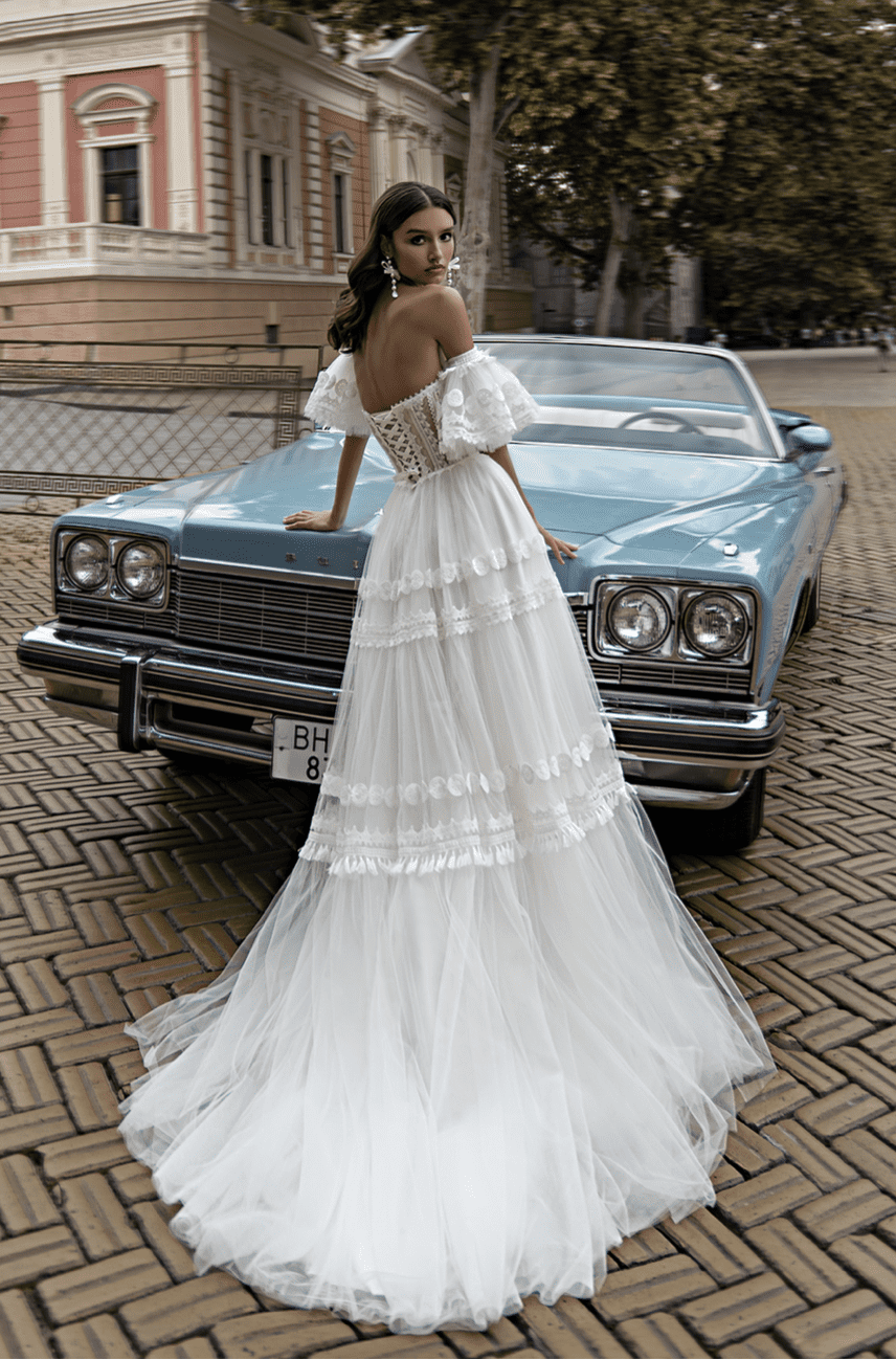A person in a white dress standing in front of a blue car Description automatically generated with medium confidence