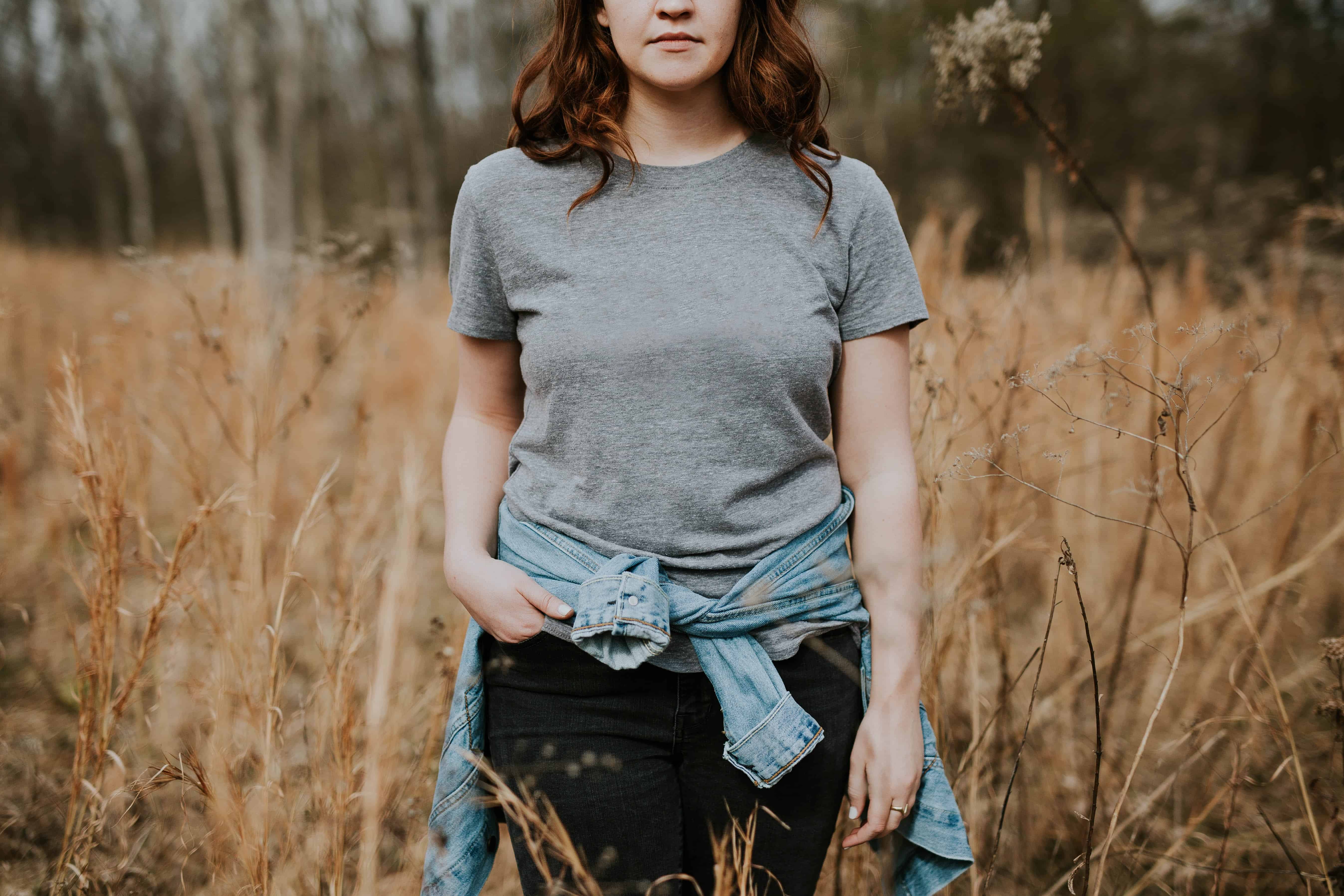 woman wearing gray crew-neck t-shirt with jacket wrap around her waist standing on brown grass field during daytime