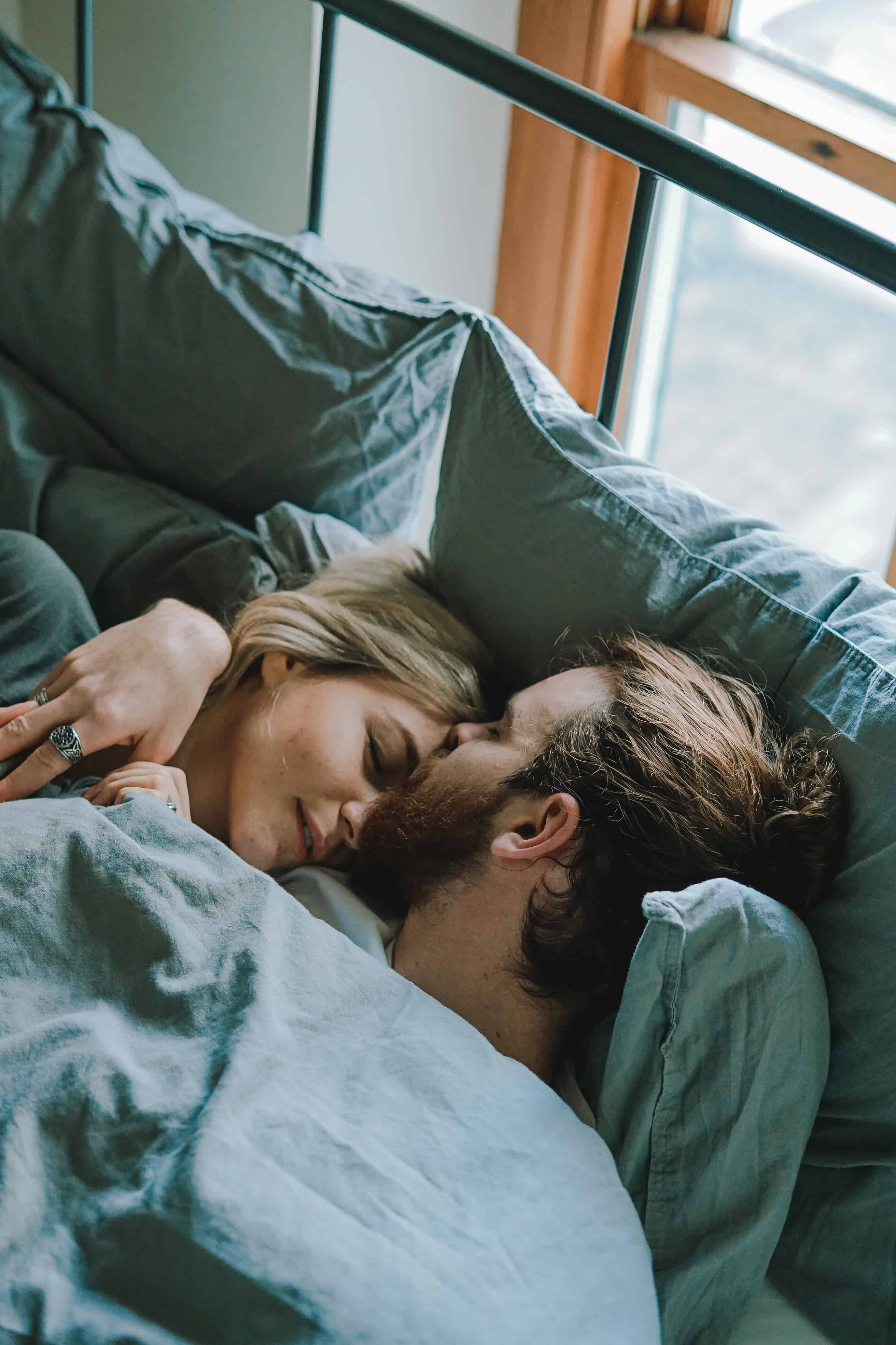 man kissing woman's forehead while lying on bed